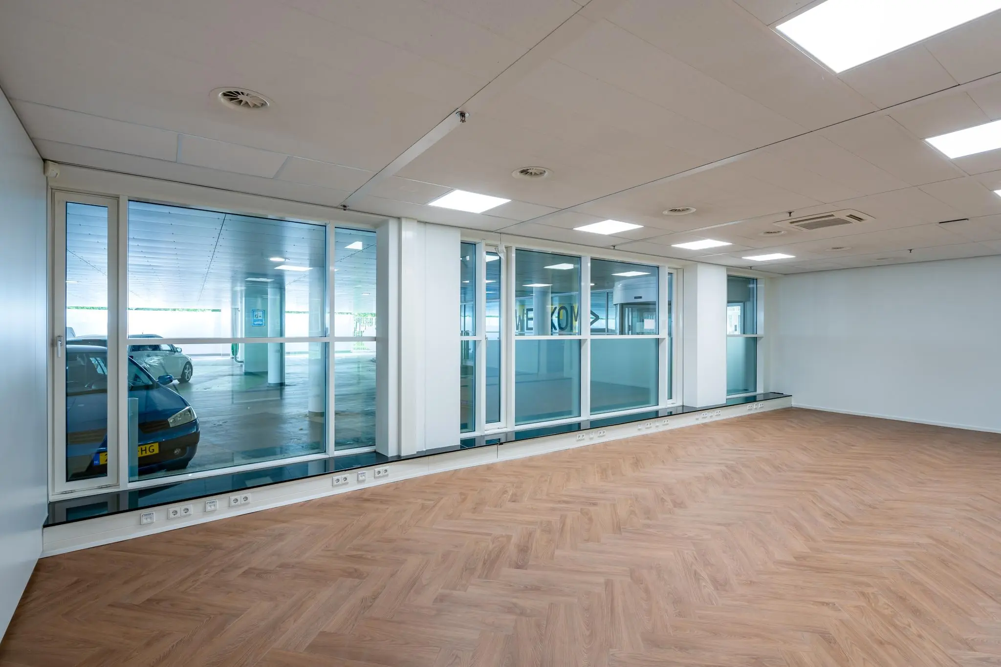 Leeg kantoorpand aan de Newtonlaan met glazen wand uitkijkend op een parkeergarage.