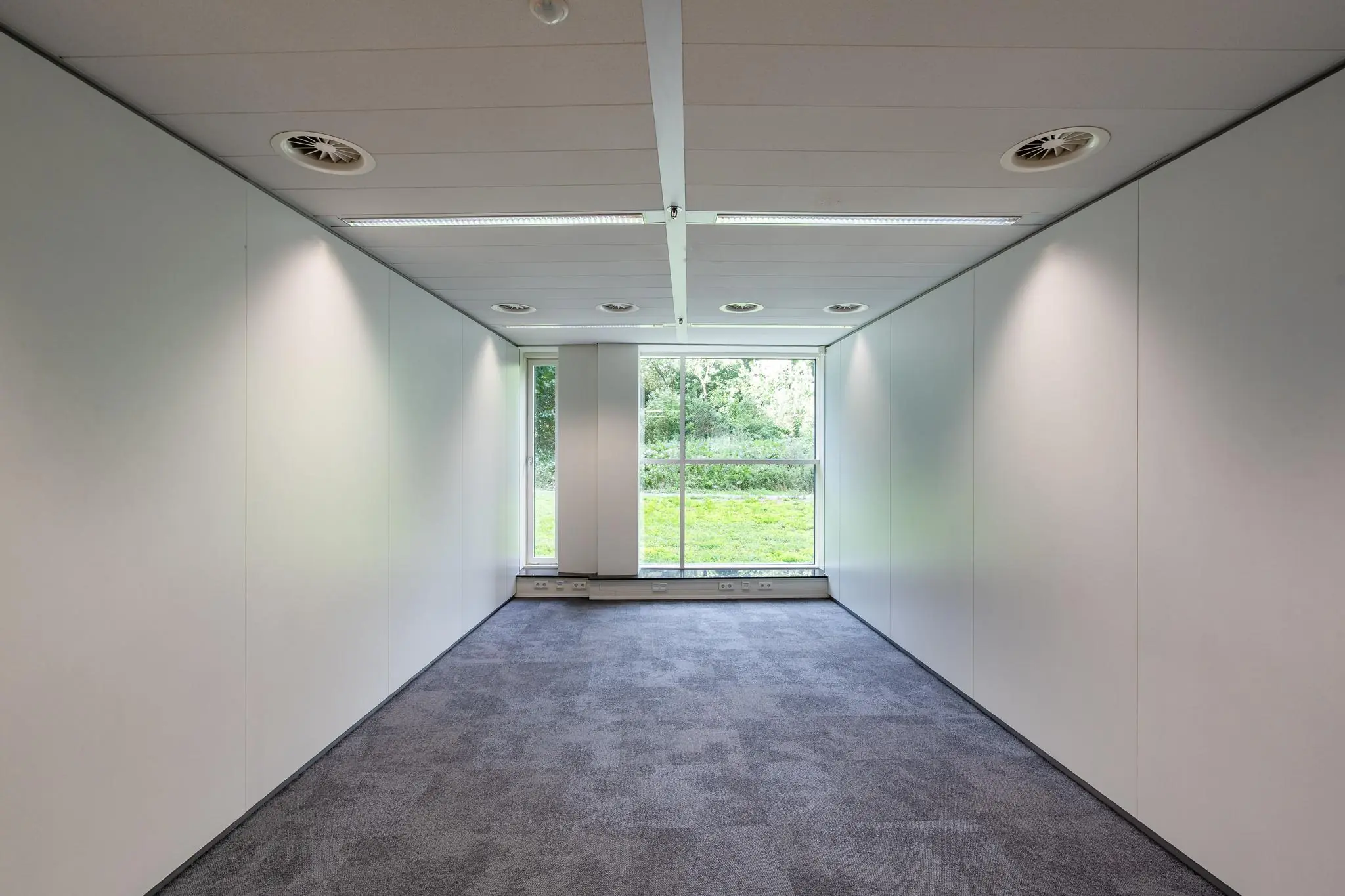Leeg kantoorruimte aan de Newtonlaan met witte wanden, grijs tapijt en een groot raam met uitzicht op groen.