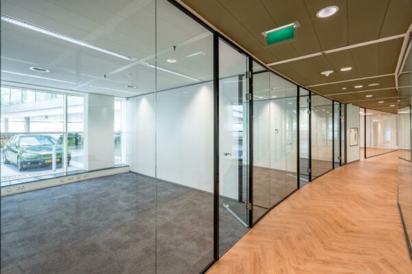 Moderne kantoorruimte aan de Newtonlaan met glazen wanden, houtlook vloer en uitzicht op een parkeerplaats.