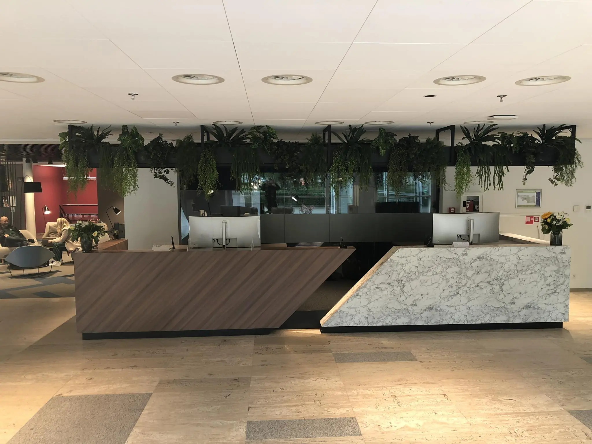 Moderne receptiebalie met hout en marmer in het kantoor aan de Newtonlaan, met hangende planten erboven.