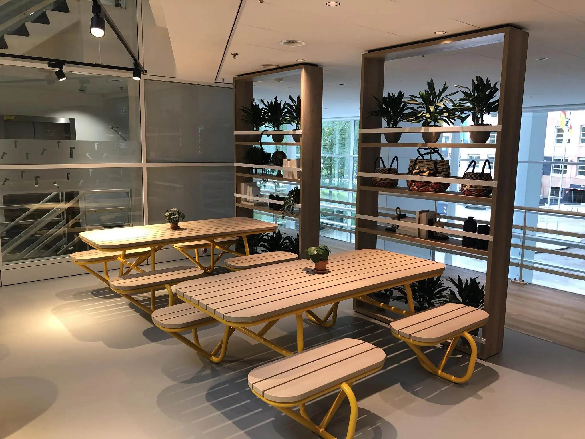 Moderne zithoek met houten picknicktafels en gele poten in een kantoor aan de Newtonlaan.