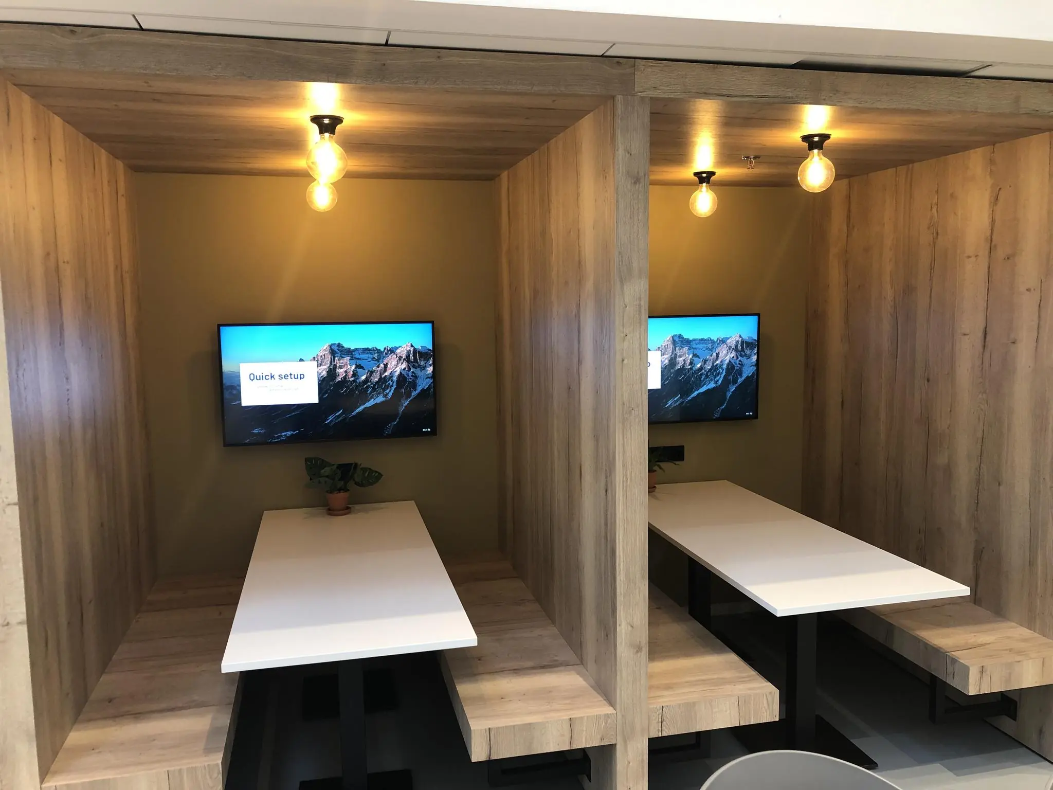 Twee houten werkpods met witte tafels, ingebouwde bankjes en beeldschermen aan de muur in een kantoor aan de Newtonlaan.