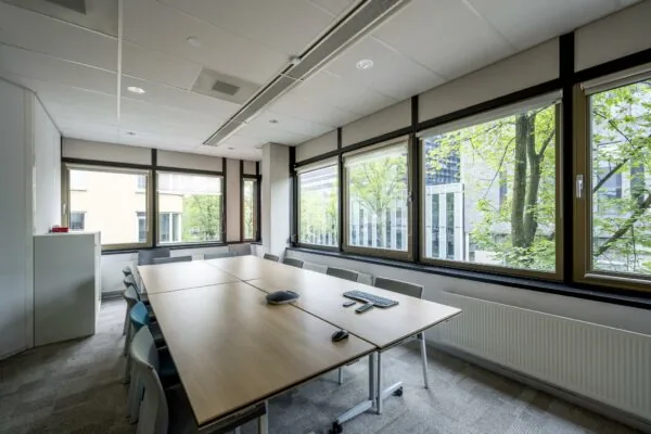 Vergaderruimte aan de Sarphatistraat met grote ramen en uitzicht op groene bomen.