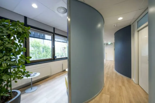 Moderne gang en wachtruimte in een kantoorpand aan de Sarphatistraat met gebogen wanden en grote ramen.