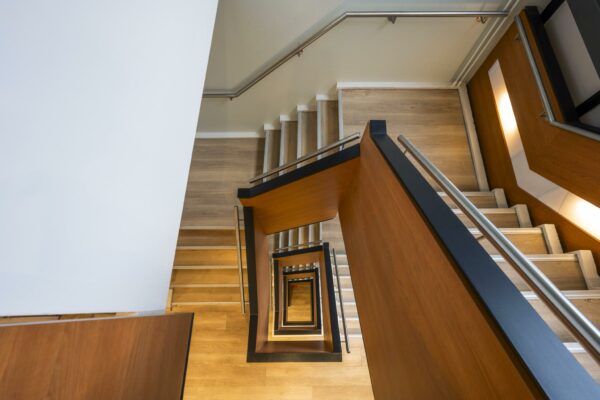 Trap met houten leuning en metalen relingen in een modern trappenhuis aan de Sarphatistraat.