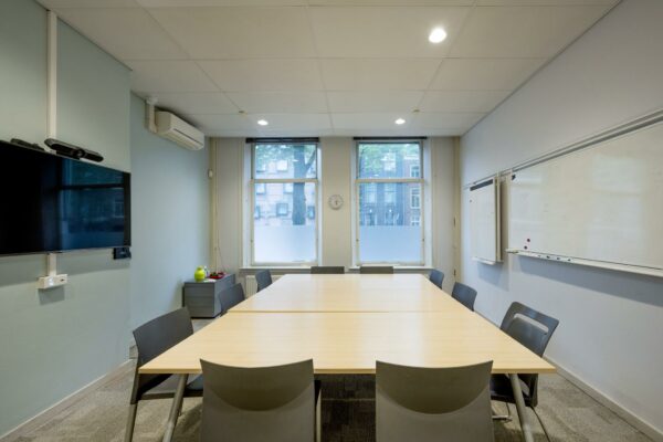 Vergaderruimte aan de Sarphatistraat met een grote tafel, stoelen, whiteboard en een flatscreen aan de muur.