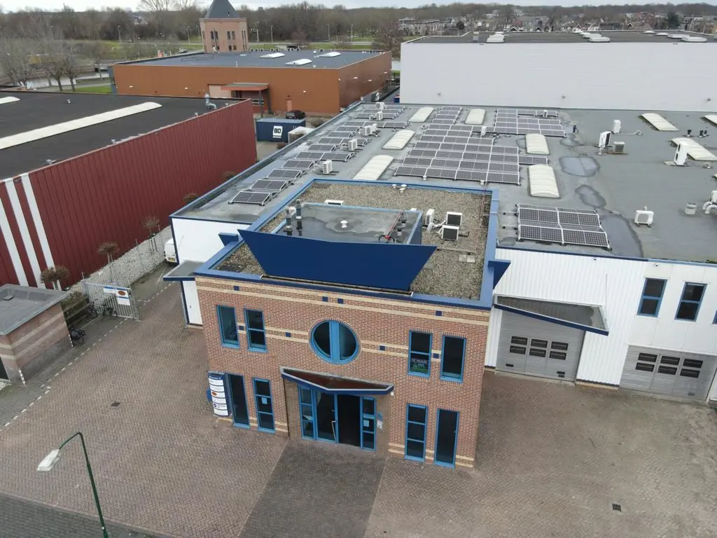 Luchtfoto van het bedrijfsgebouw aan de Bergveste met zonnepanelen op het dak en een bakstenen voorgevel met blauwe accenten.