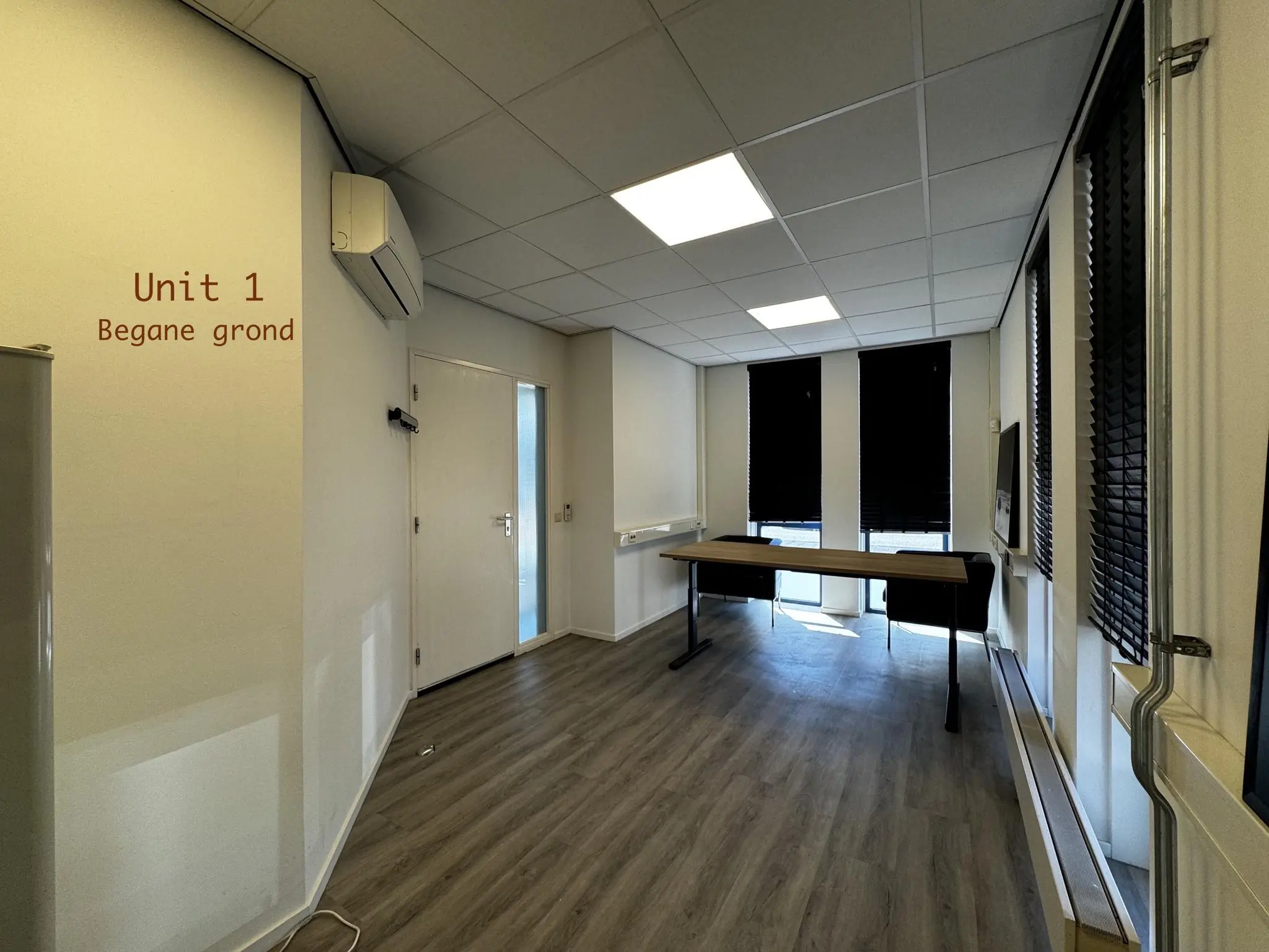 Kantoorruimte Unit 1 op de begane grond met een bureau, stoelen en verduisterde ramen.