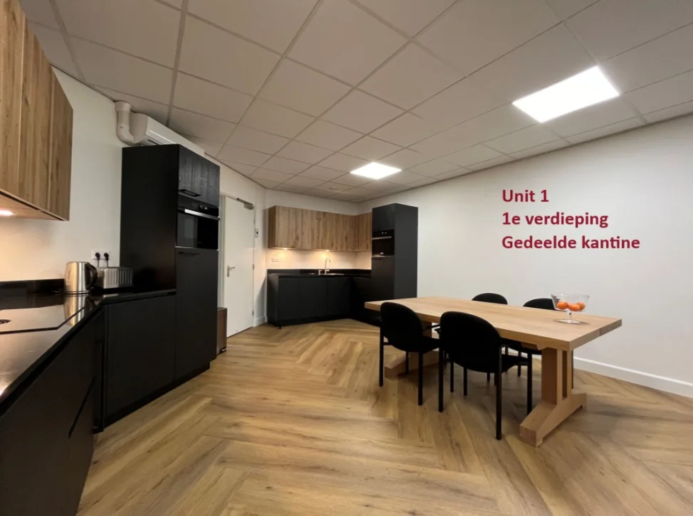Moderne gedeelde kantine op de eerste verdieping van Unit 1 met een houten eettafel, zwarte keuken en houtaccenten.