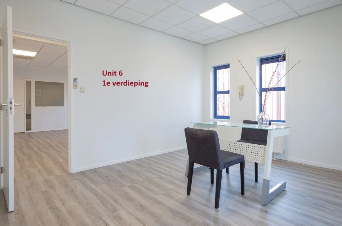 Lichte kantoorruimte op de eerste verdieping (Unit 6) met een glazen bureau, twee stoelen en twee ramen.