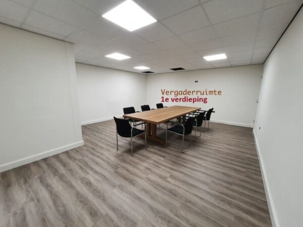Vergaderruimte op de eerste verdieping met een grote houten tafel en zwarte stoelen in een modern interieur.
