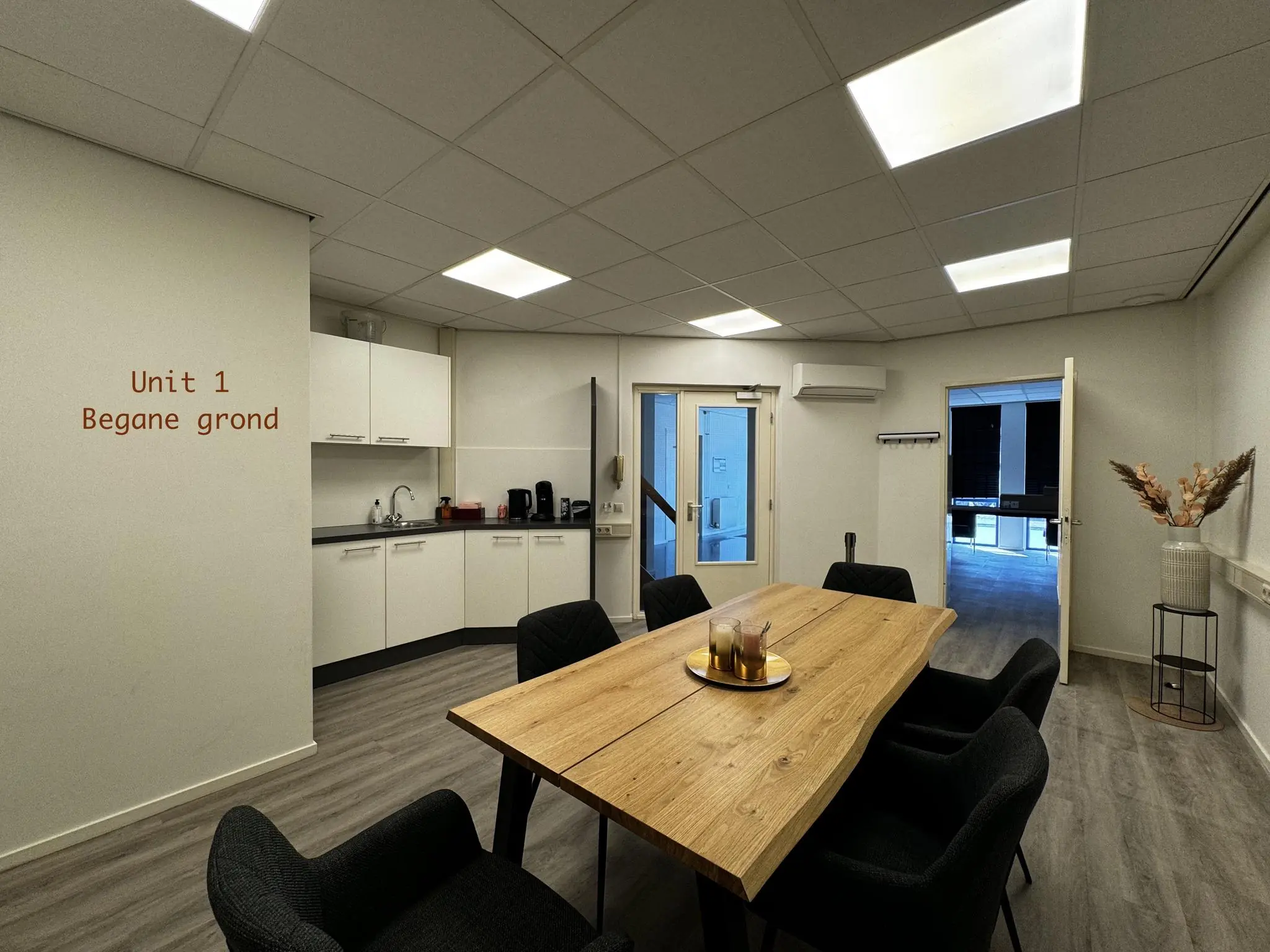 Vergaderruimte met houten tafel, zithoek, pantry en opschrift "Unit 1 Begane grond" op de muur.