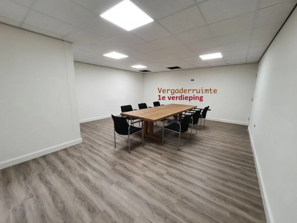 Vergaderruimte op de eerste verdieping met houten tafel en zwarte stoelen in een moderne, minimalistische stijl.