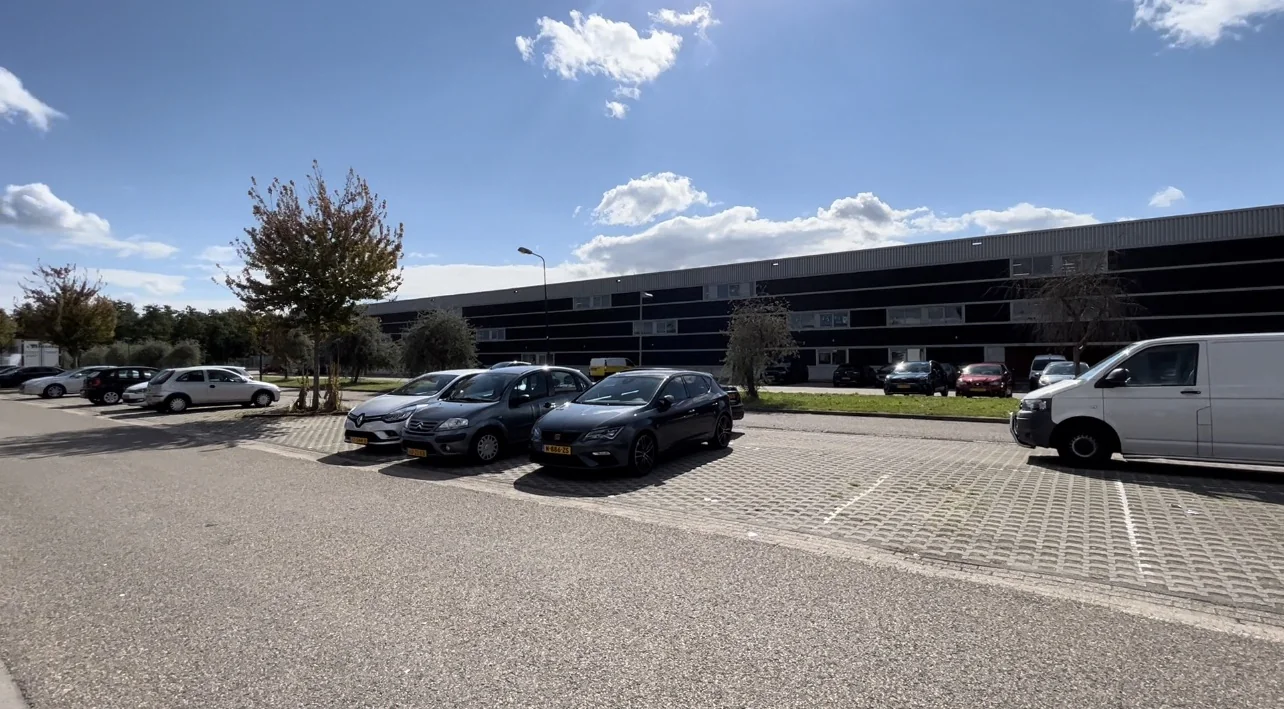 Parkeerplaats met geparkeerde auto's voor het bedrijfsgebouw Bergveste op een zonnige dag.