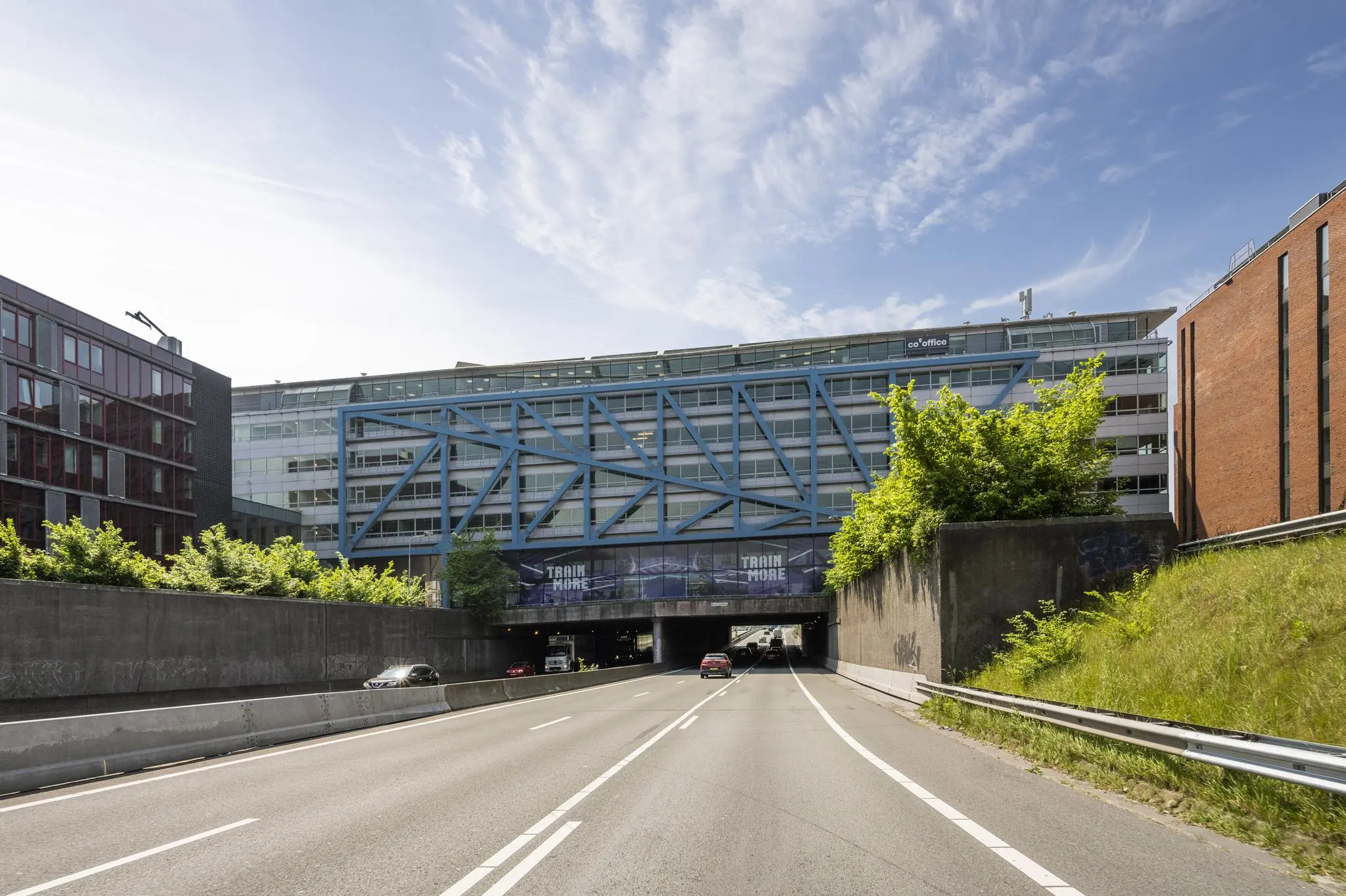 Zicht op het Bos en Lommerplein in Amsterdam met een gebouw boven een tunnel en auto's op de weg.