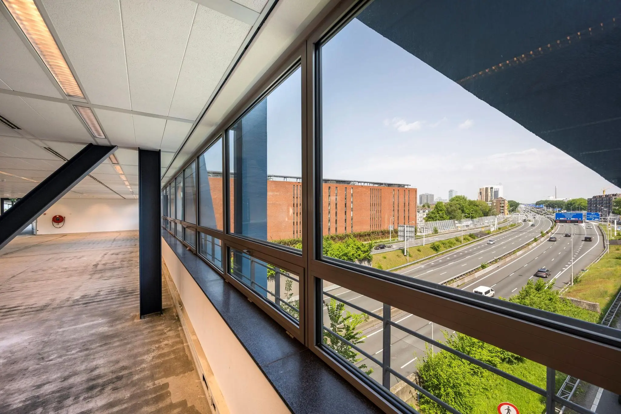 Uitzicht vanuit een leeg kantoor aan het Bos en Lommerplein op de snelweg en een groot rood bakstenen gebouw.