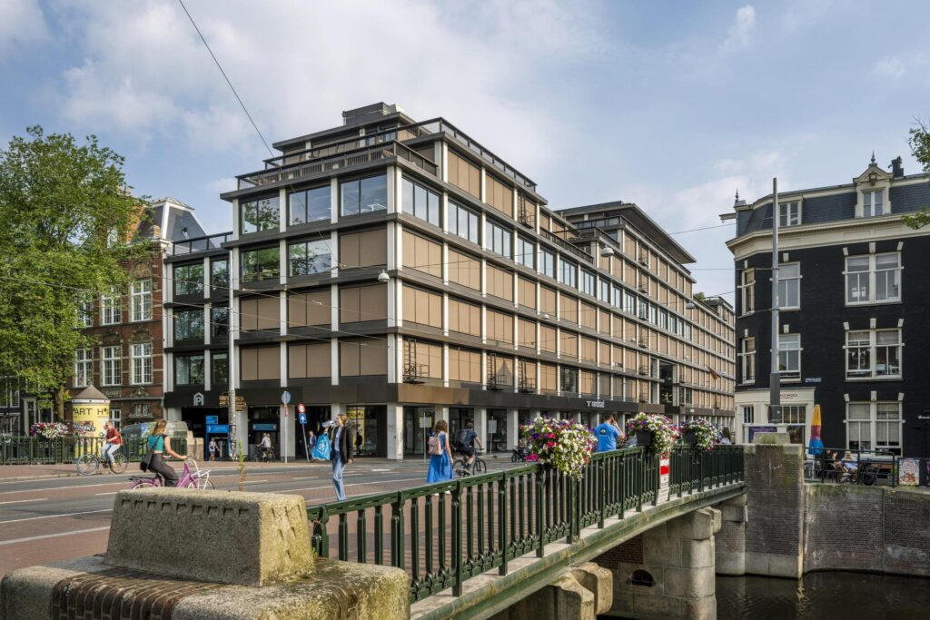 Straatbeeld van de Vijzelstraat in Amsterdam met moderne en klassieke gebouwen, zichtbaar vanaf een brug over een gracht.