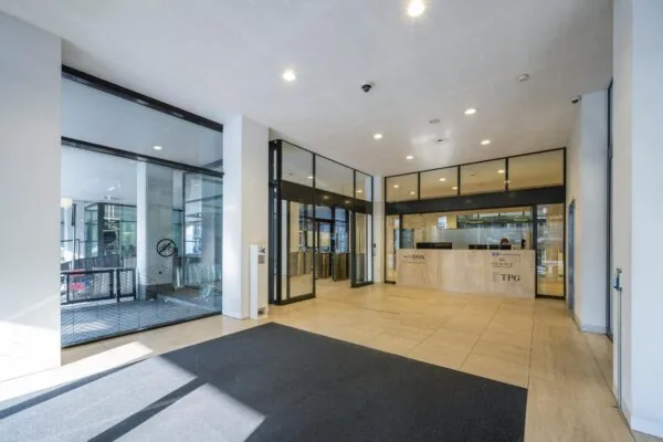 Moderne, lichte entreehal van een kantoorpand aan de Vijzelstraat met een receptiebalie en glazen deuren.