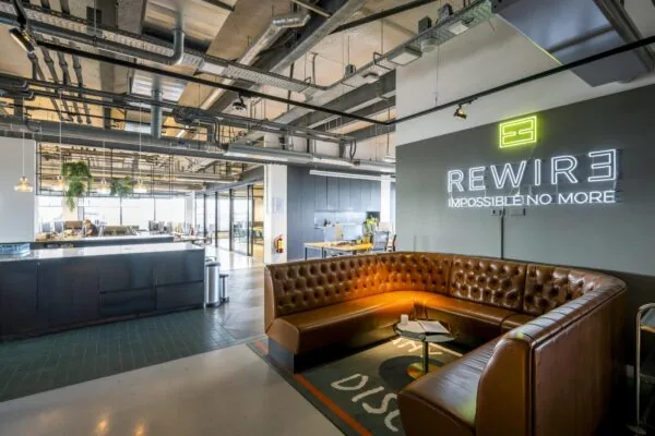 Moderne kantoorruimte aan de Vijzelstraat met een leren zithoek, neonbord "REWIRE" en industriële plafondafwerking.