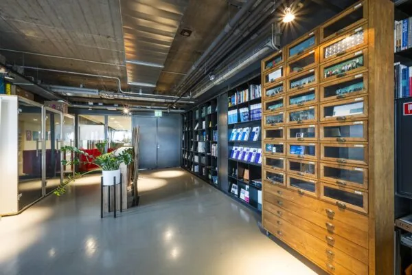 Moderne kantoorruimte aan de Vijzelstraat met industriële plafonds, een houten vitrinekast en een wand vol boeken en tijdschriften.
