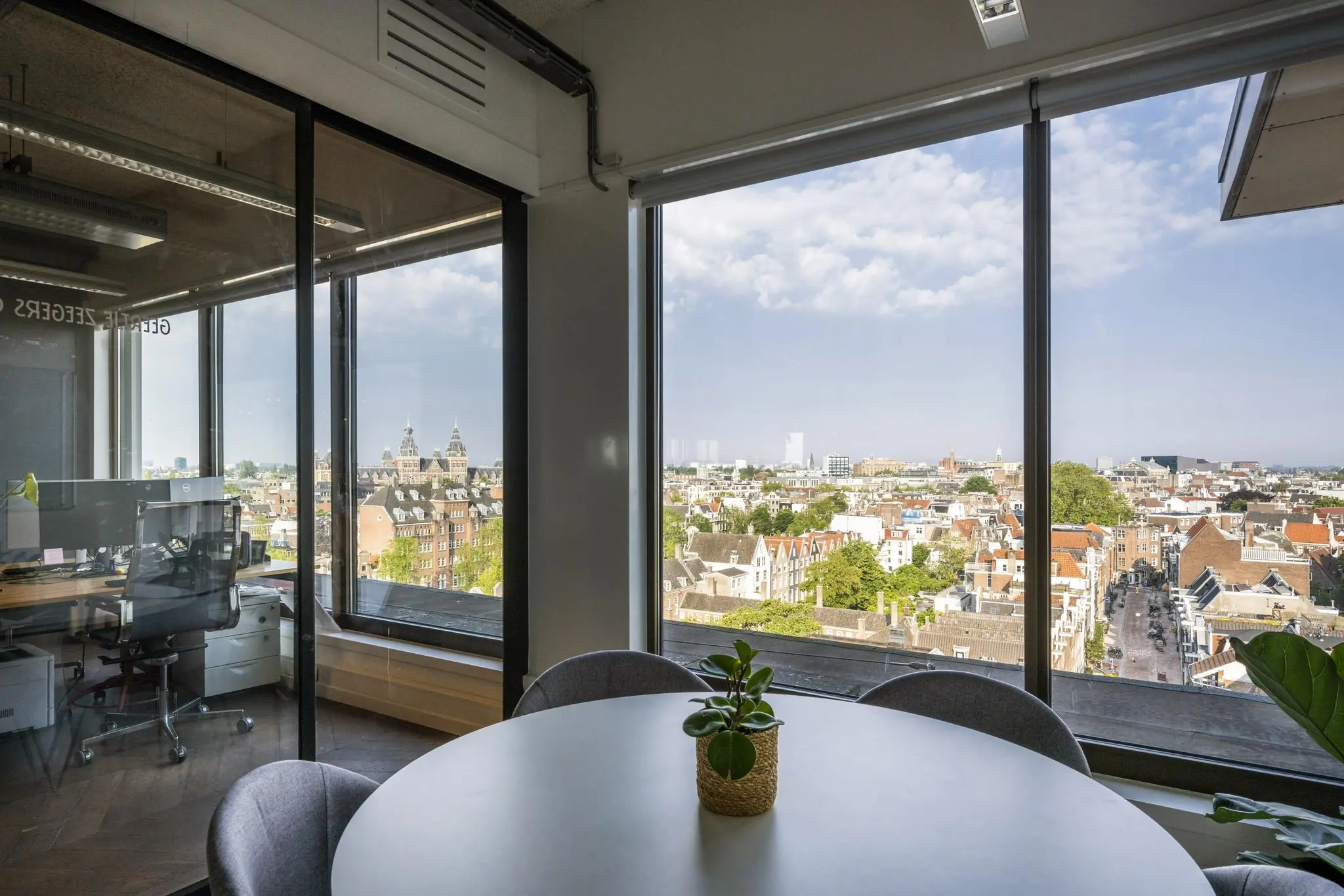 Modern kantoorinterieur met ronde vergadertafel en uitzicht op de Amsterdamse binnenstad vanaf de Vijzelstraat.