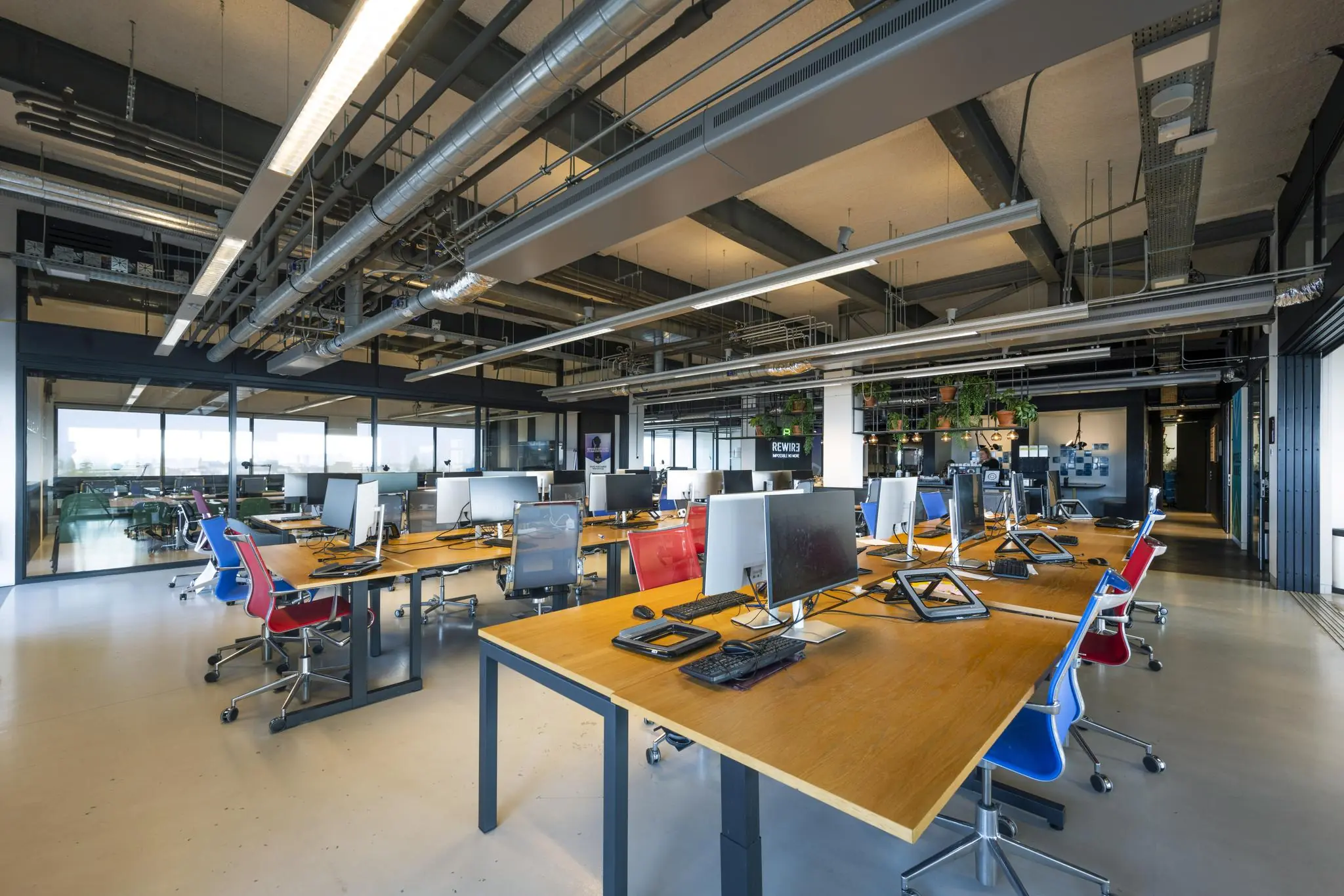 Moderne en open kantooruimte aan de Vijzelstraat met grote houten bureaus, kleurrijke stoelen en werkplekken met computers.