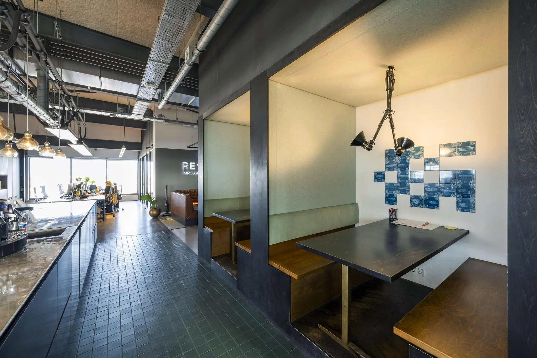 Moderne kantoorruimte aan de Vijzelstraat met open werkplekken, een zithoek en een afgesloten vergaderruimte met wandlamp en blauwe tegels.
