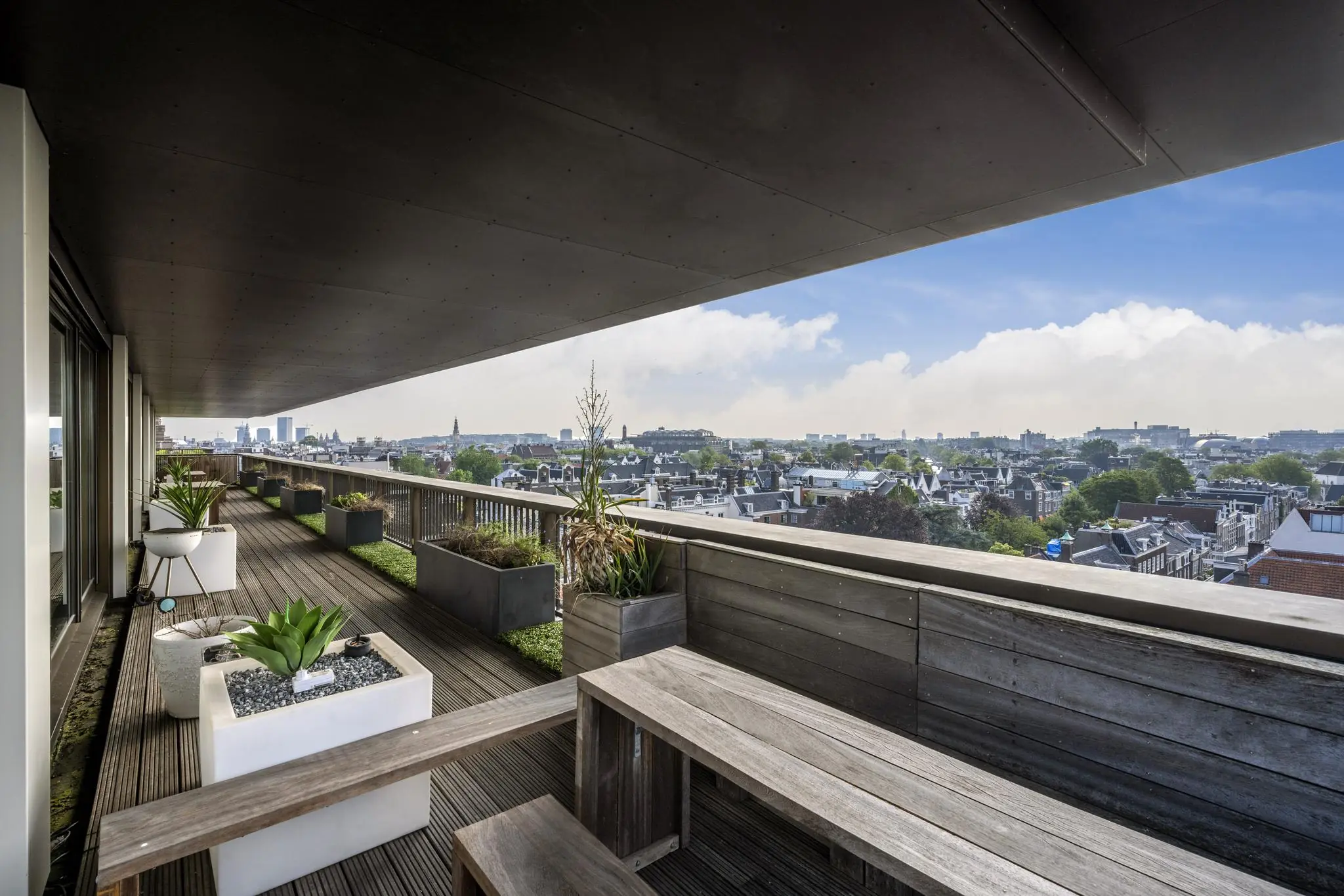 Ruim balkon aan de Vijzelstraat met houten vlonders, plantenbakken en uitzicht over de Amsterdamse binnenstad.