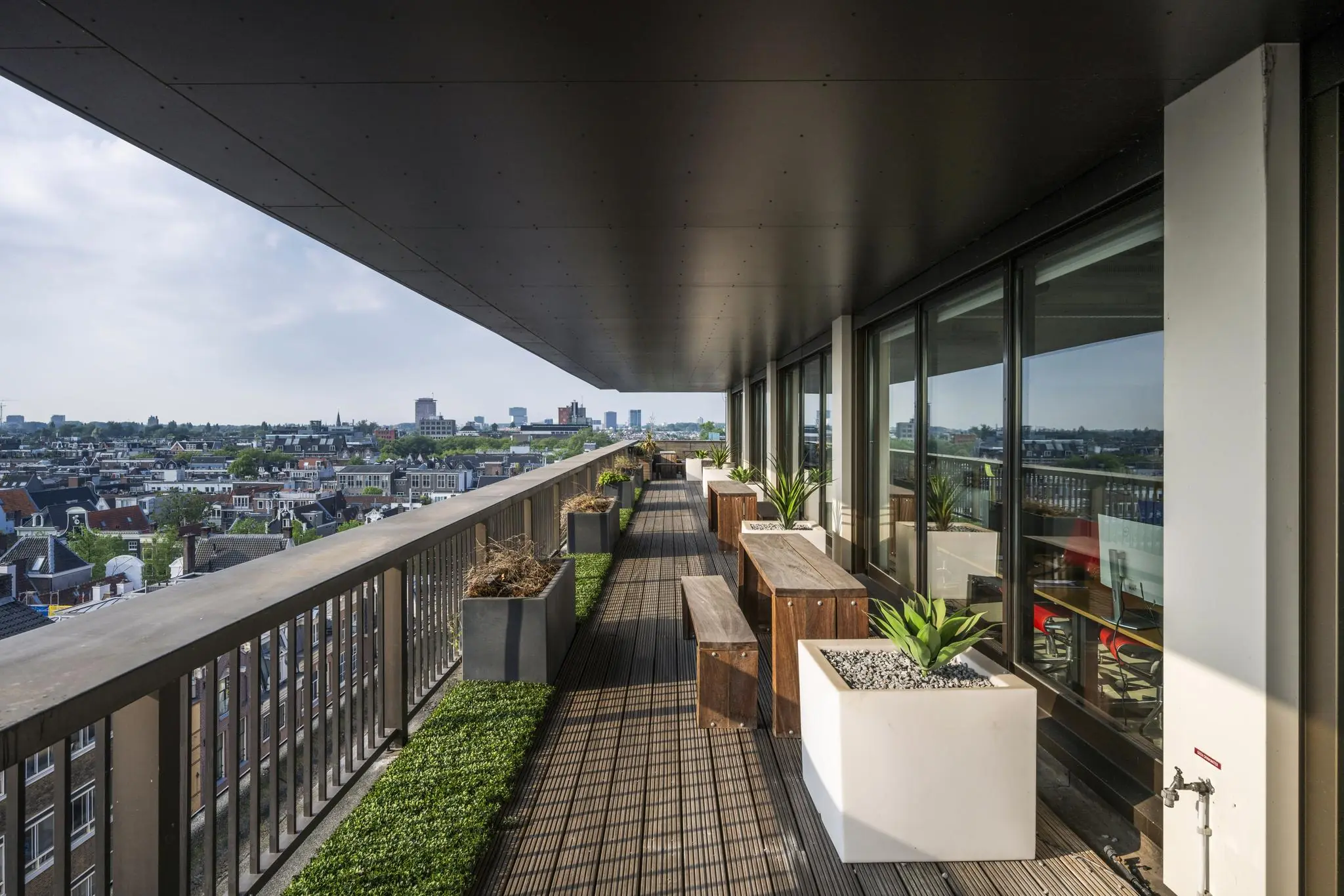 Ruim balkon aan de Vijzelstraat met houten zitbanken, plantenbakken en uitzicht over de stad.