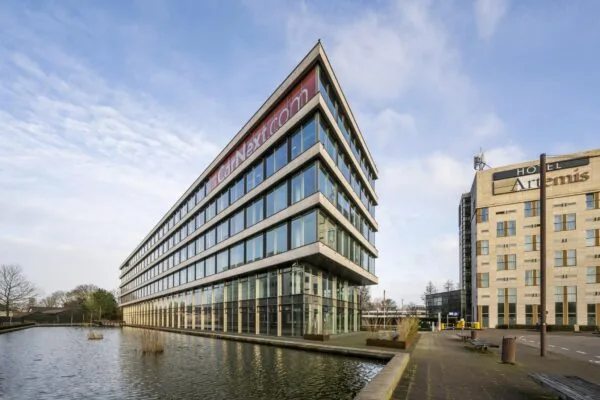 Modern kantoorgebouw van CarNext.com bij een waterpartij, met Hotel Artemis op de achtergrond aan het John M. Keynesplein.