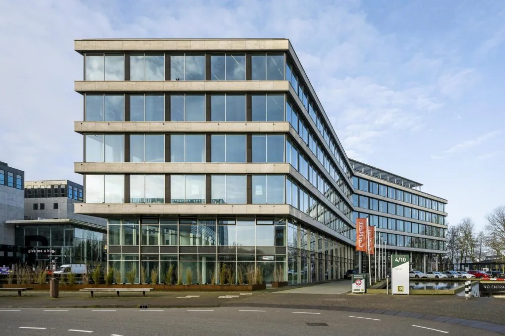 Modern kantoorgebouw aan het John M. Keynesplein met glazen gevels en parkeerplaatsen aan de voorzijde.