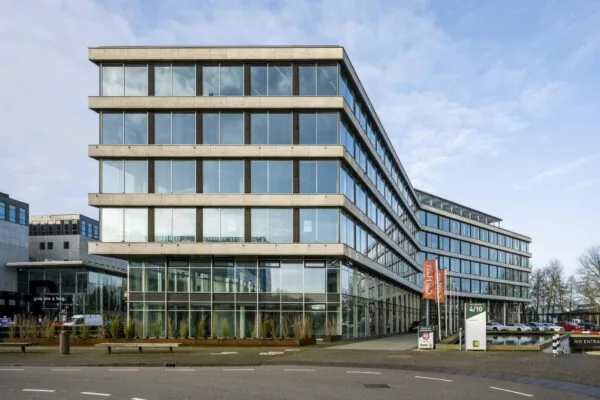 Modern kantoorgebouw aan het John M. Keynesplein met glazen gevels en parkeerplaatsen aan de voorzijde.