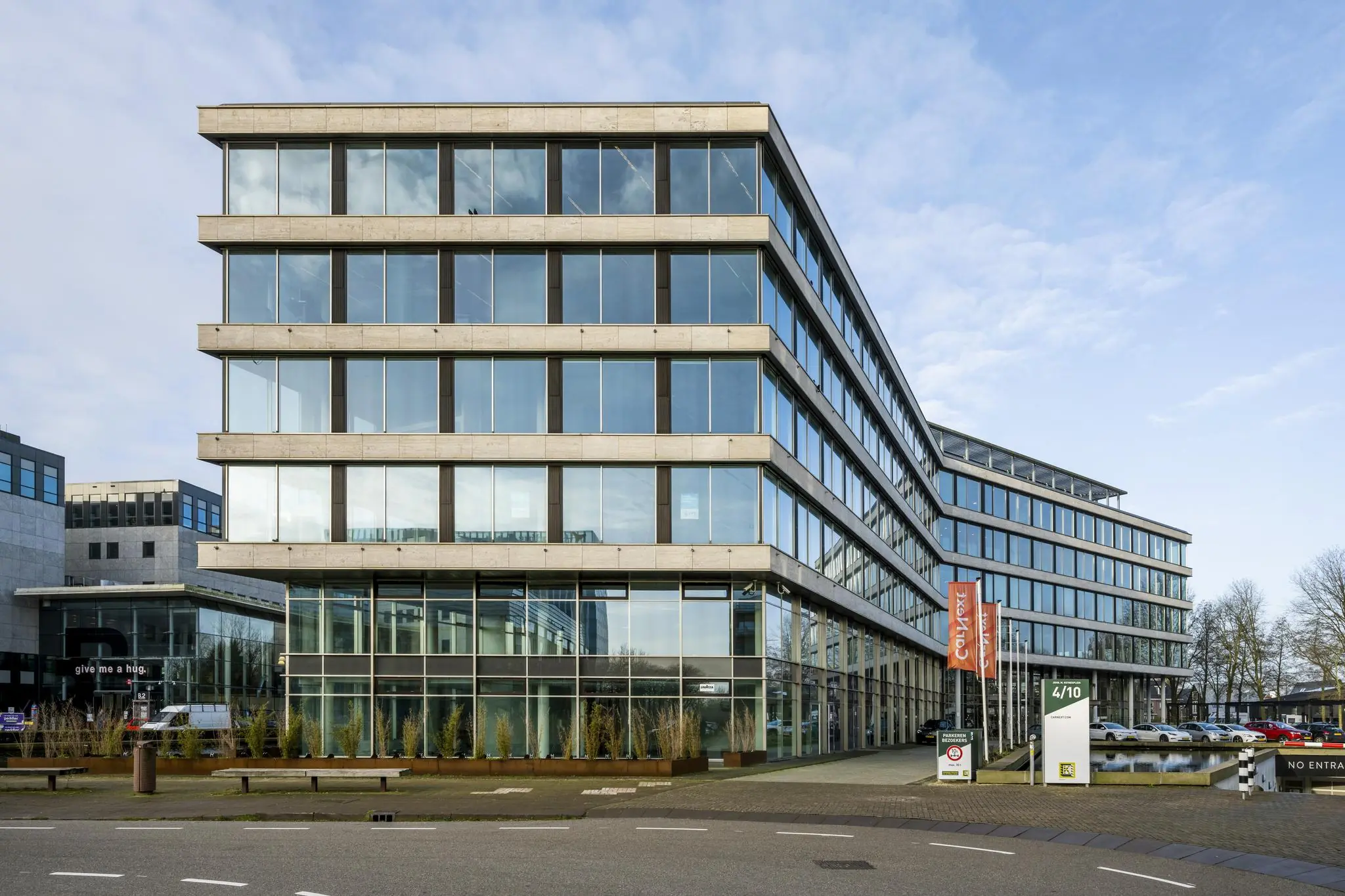 Modern kantoorgebouw aan het John M. Keynesplein met glazen gevels en parkeerplaatsen aan de voorzijde.