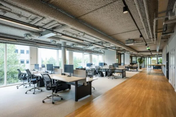 Moderne open kantoorruimte aan het John M. Keynesplein met bureaus, bureaustoelen en computers, omgeven door grote ramen.