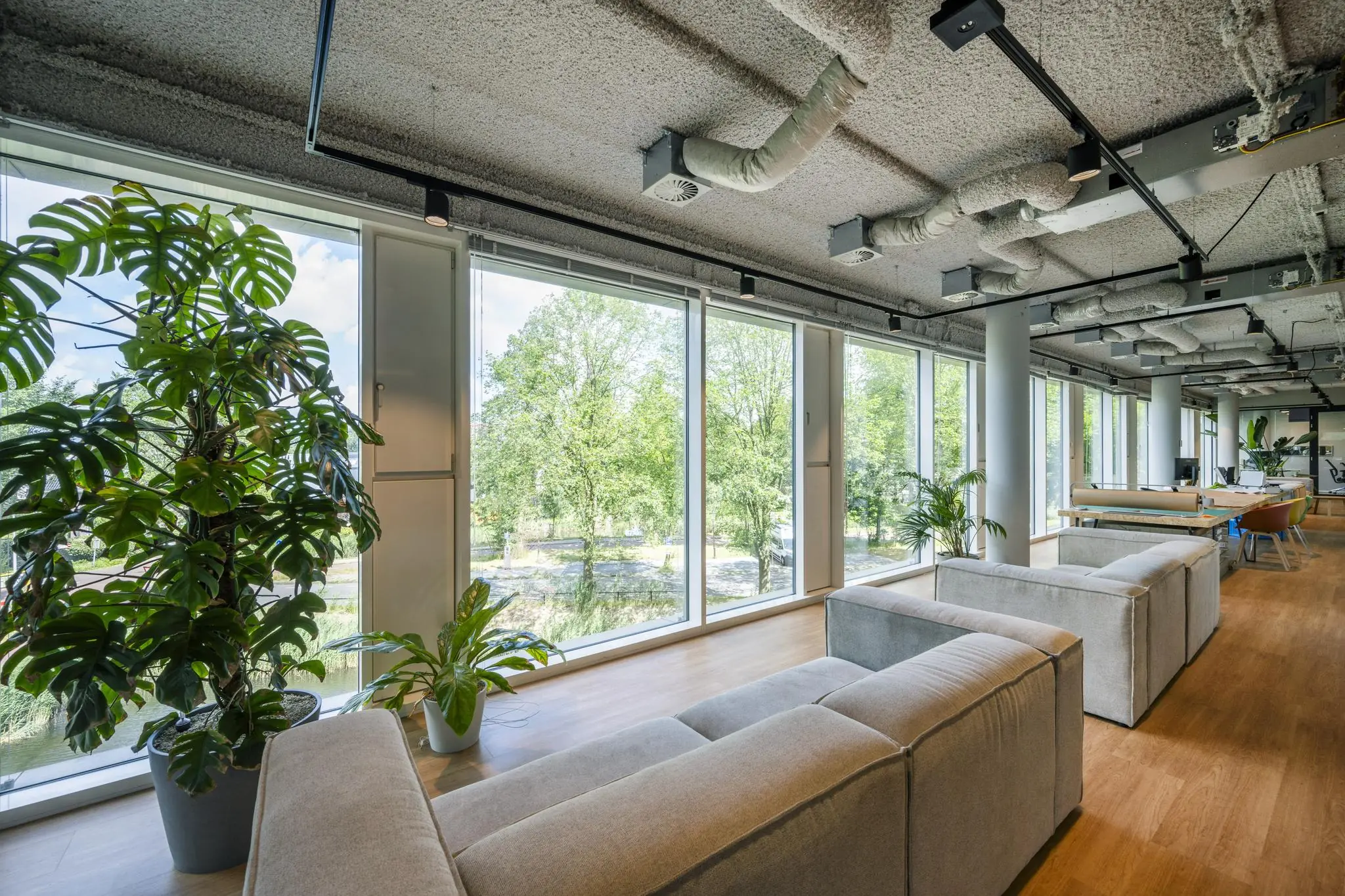 Moderne kantoorruimte aan het John M. Keynesplein met grote ramen, groen uitzicht, comfortabele zitbanken en veel planten.