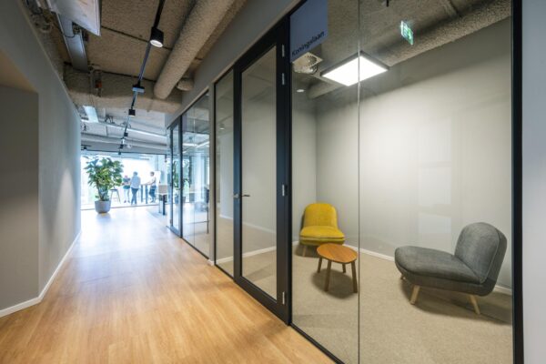 Moderne kantoorruimte aan het John M. Keynesplein met glazen vergaderruimtes en een zitje met gele en grijze stoelen.