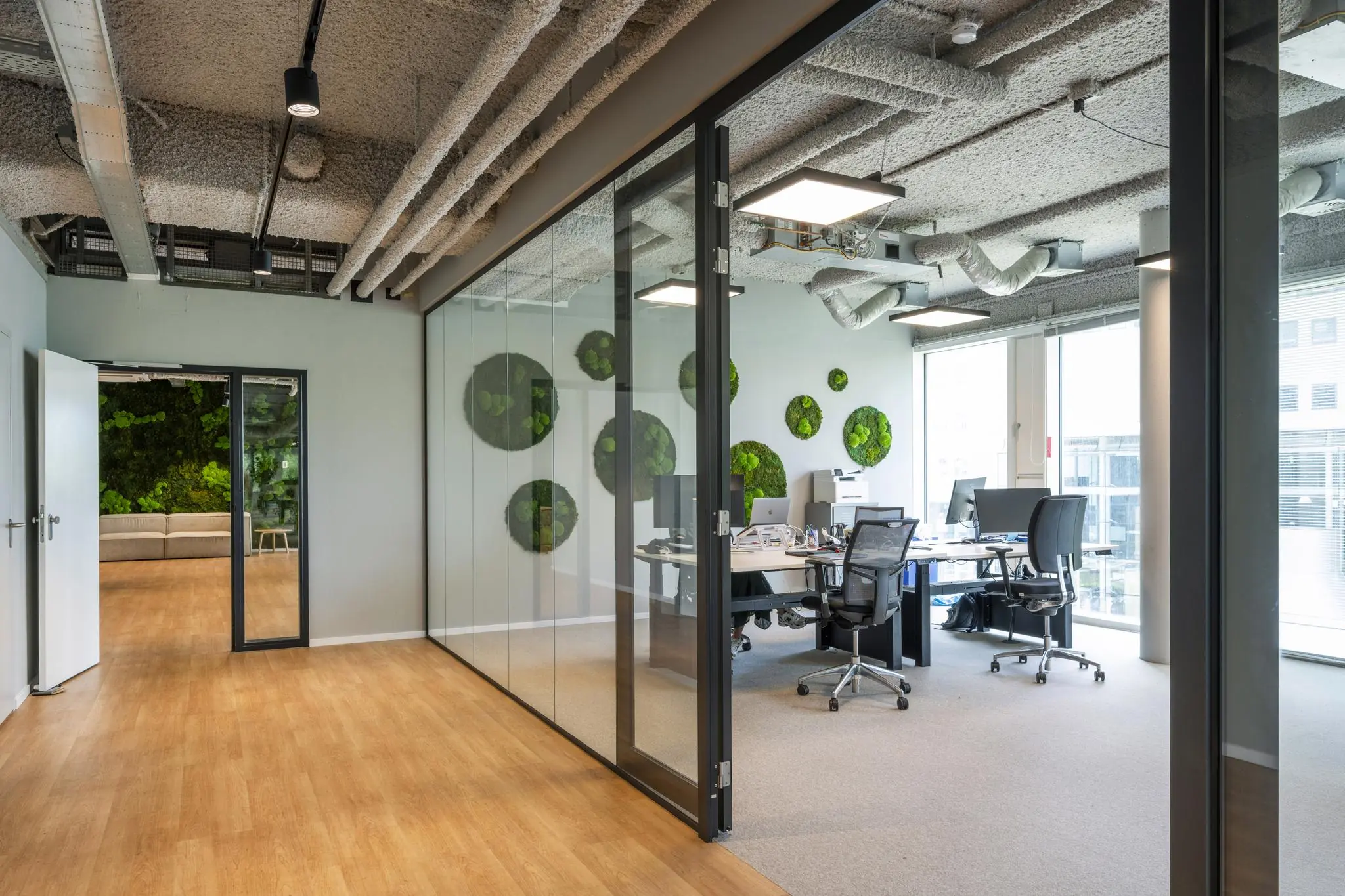 Modern kantoorinterieur aan het John M. Keynesplein met glazen wanden, bureaus en groene wanddecoratie.