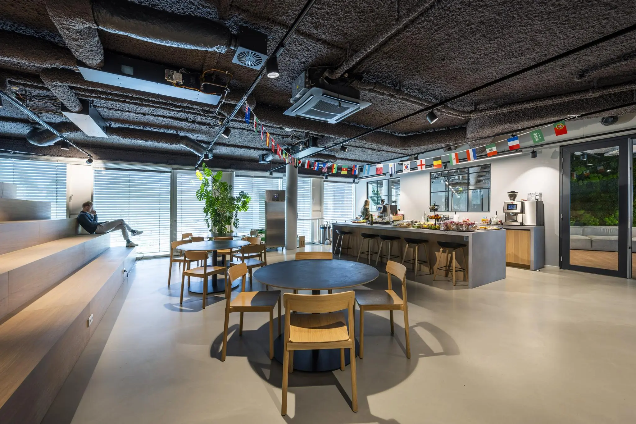 Moderne, open kantoorruimte aan het John M. Keynesplein met zitgedeelte, keukeneiland en internationale vlaggen aan het plafond.