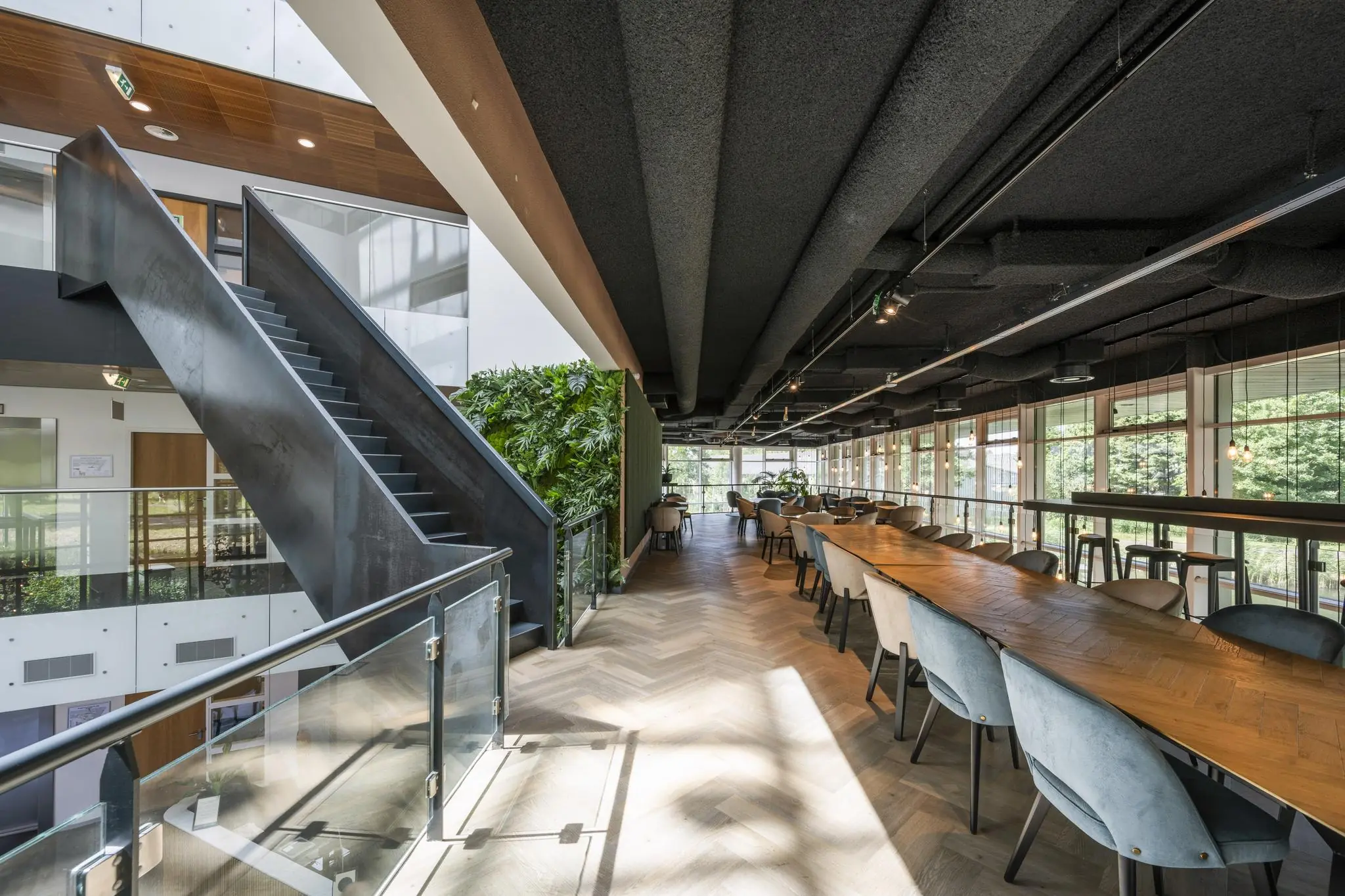 Modern kantoorinterieur aan het John M. Keynesplein met lange houten vergadertafel, groene wand en industriële trap.