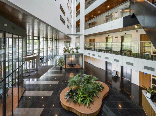 Moderne kantoorhal aan het John M. Keynesplein met zitgedeelte, veel glas en groenvoorziening.
