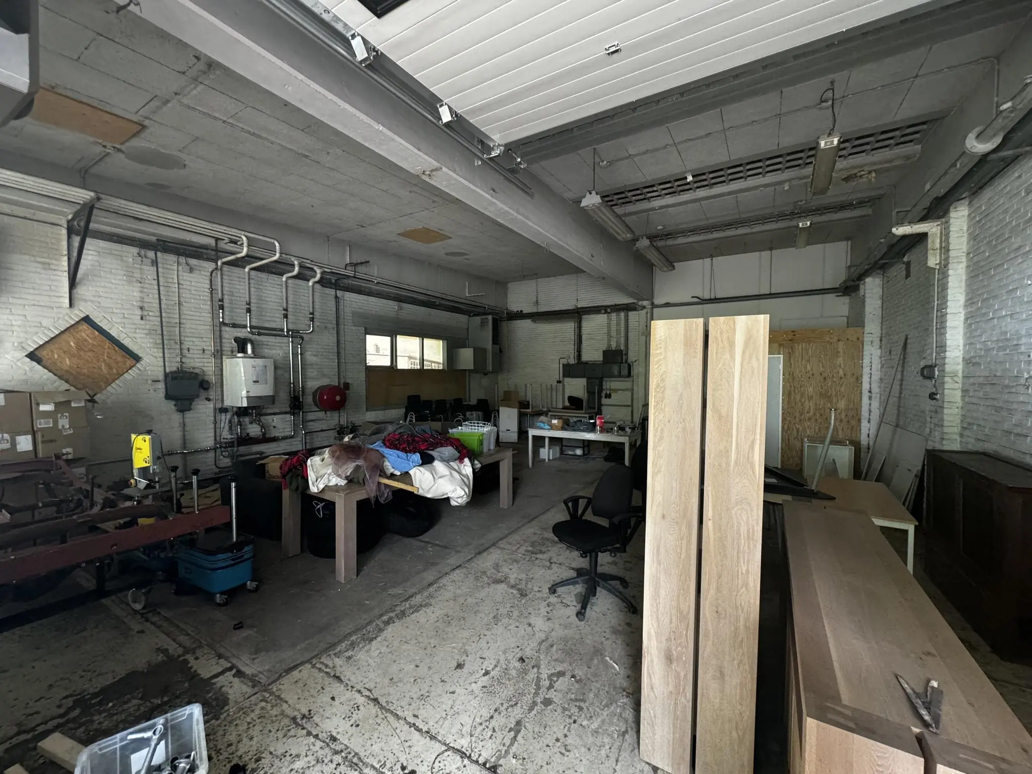 Een rommelige werkplaats in een loods aan de Lekdijk, met houten panelen, werktafels en diverse gereedschappen en materialen.