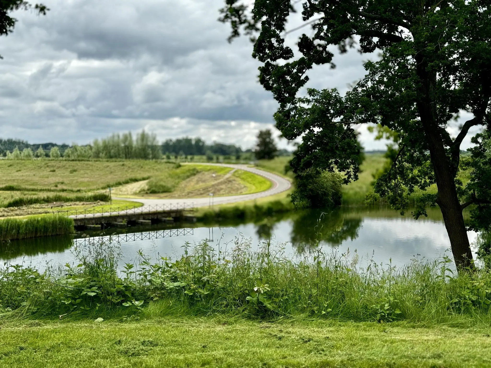 Rustiek landschap bij de Lekdijk met een kronkelende weg, brug en weerspiegeling in het water.