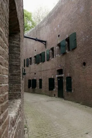Binnenplaats van een oud fort aan de Lekdijk met hoge bakstenen muren en gesloten groene luiken.