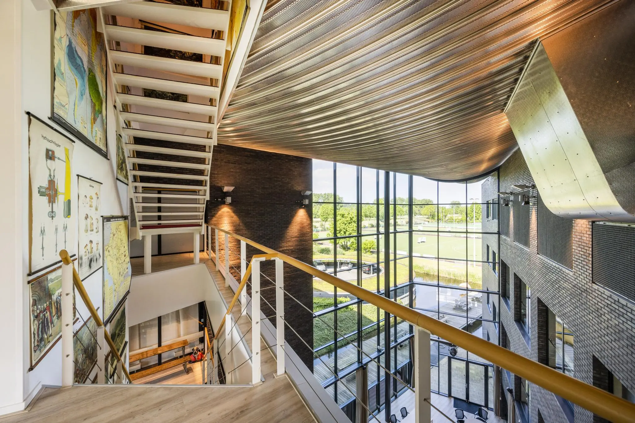 Moderne trappenhal met grote raampartijen en educatieve wandkaarten in een gebouw aan de Prof. W.H. Keesomlaan.