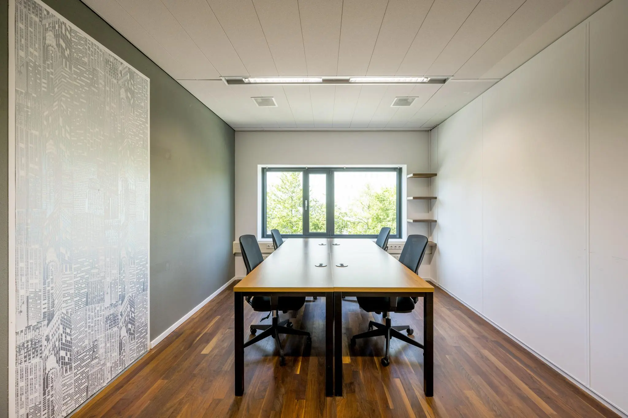 Vergaderruimte aan de Prof. W.H. Keesomlaan met houten vloer, zes stoelen, grote tafel en raam met uitzicht op groen.