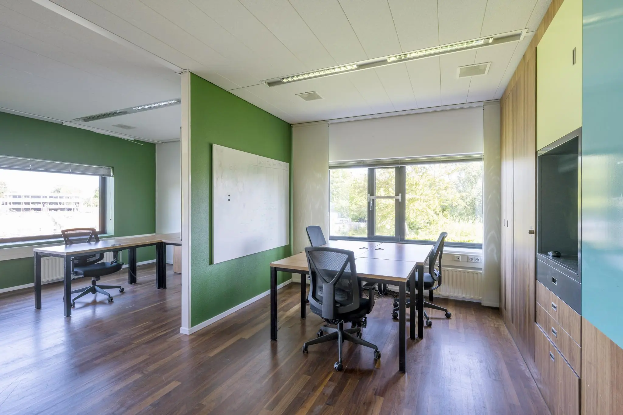 Licht en modern ingericht kantoor met meerdere bureaus, bureaustoelen, houten vloer en grote ramen aan de Prof. W.H. Keesomlaan.