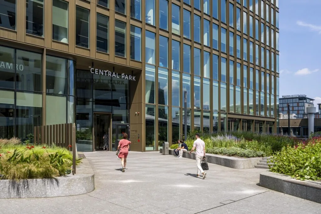 Ingang van het Central Park-gebouw aan het Stadsplateau met voorbijgangers en omliggende beplanting.