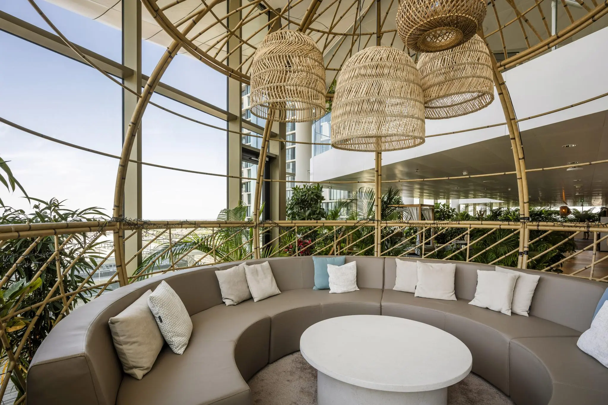 Moderne loungehoek op het Stadsplateau met ronde bank, kussens, rotanlampen en veel groen.