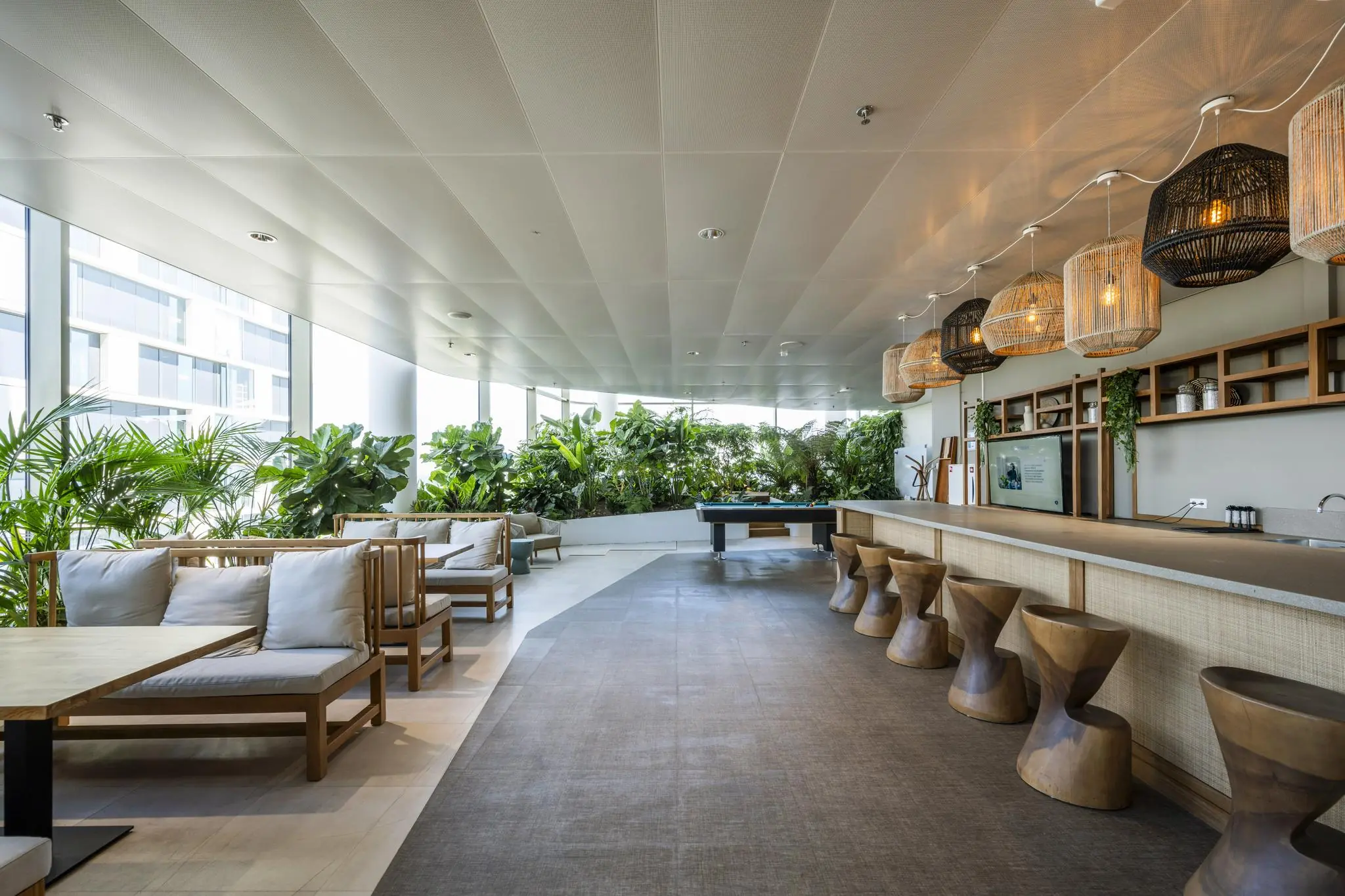 Modern gemeenschappelijk interieur met houtaccenten, veel groen, een bar en zithoeken in het Stadsplateau-gebouw.