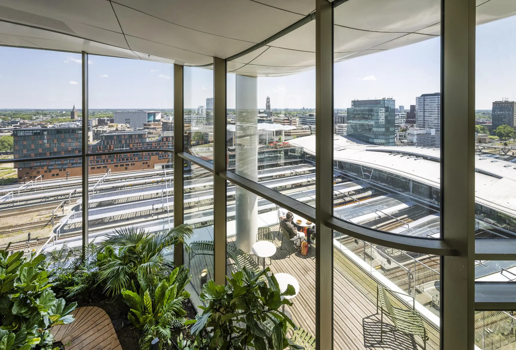 Uitzicht vanuit een modern gebouw op het Stadsplateau en station Utrecht Centraal, met een binnentuin en terras op de voorgrond.